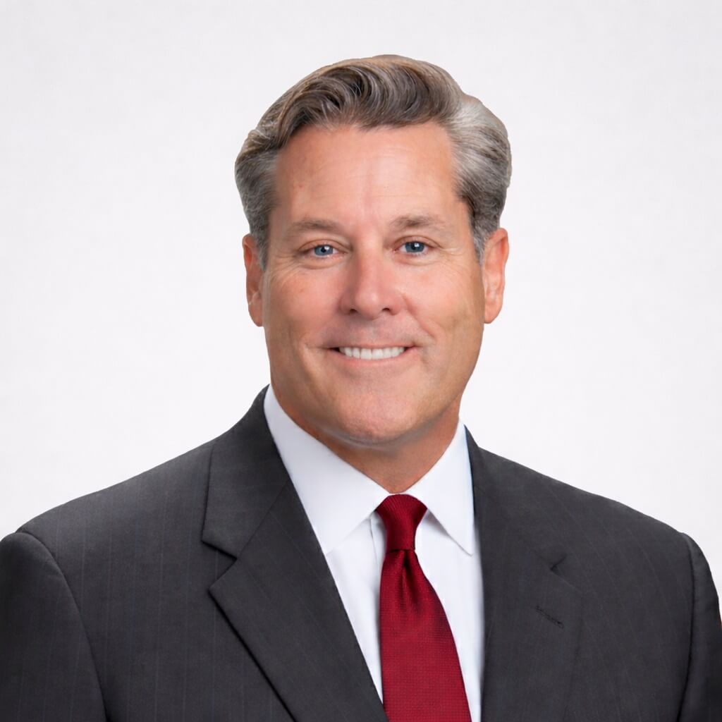 Professional headshot of a smiling middle-aged man in a suit with a red tie, set against a neutral background.